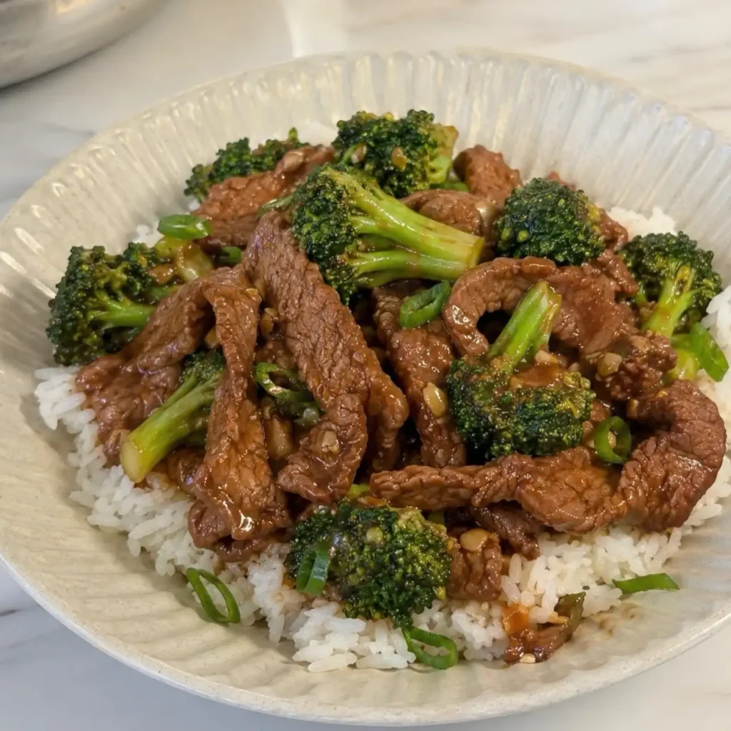 Beef and broccoli stir fry served over steamed white rice with green onions.