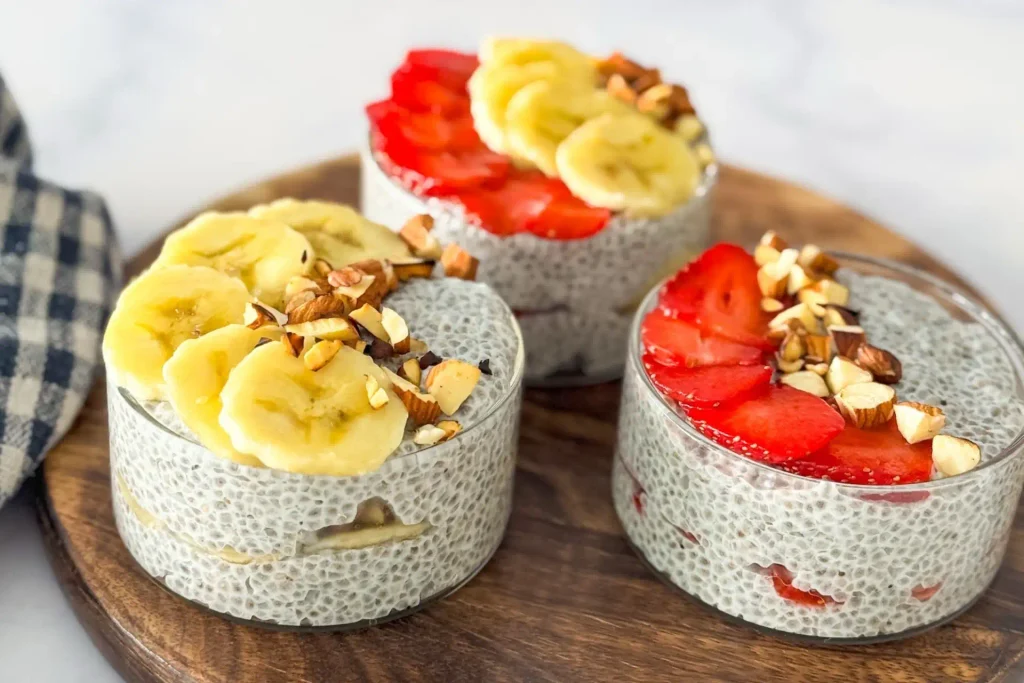 Chia Seed Pudding Recipe: Creamy 5 Ingredient No Cook 5 Chia seed pudding topped with sliced bananas, strawberries, and chopped nuts in glass cups.