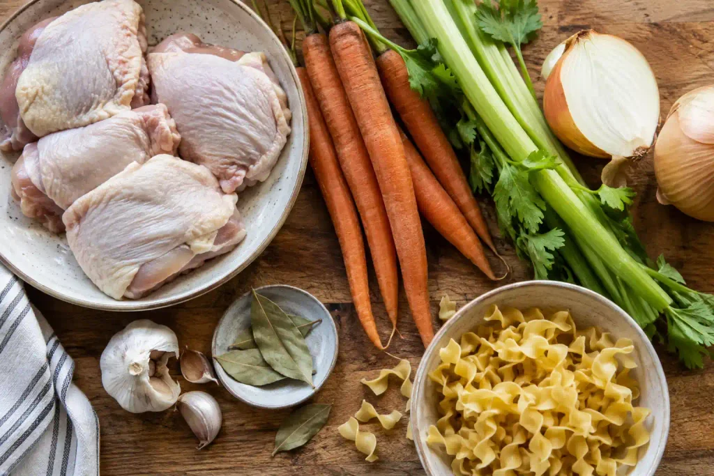 Chicken Noodle Soup Recipe: A Hearty Broth Ready in 60 Minutes 3 Raw ingredients for easy chicken noodle soup laid out on a wooden board