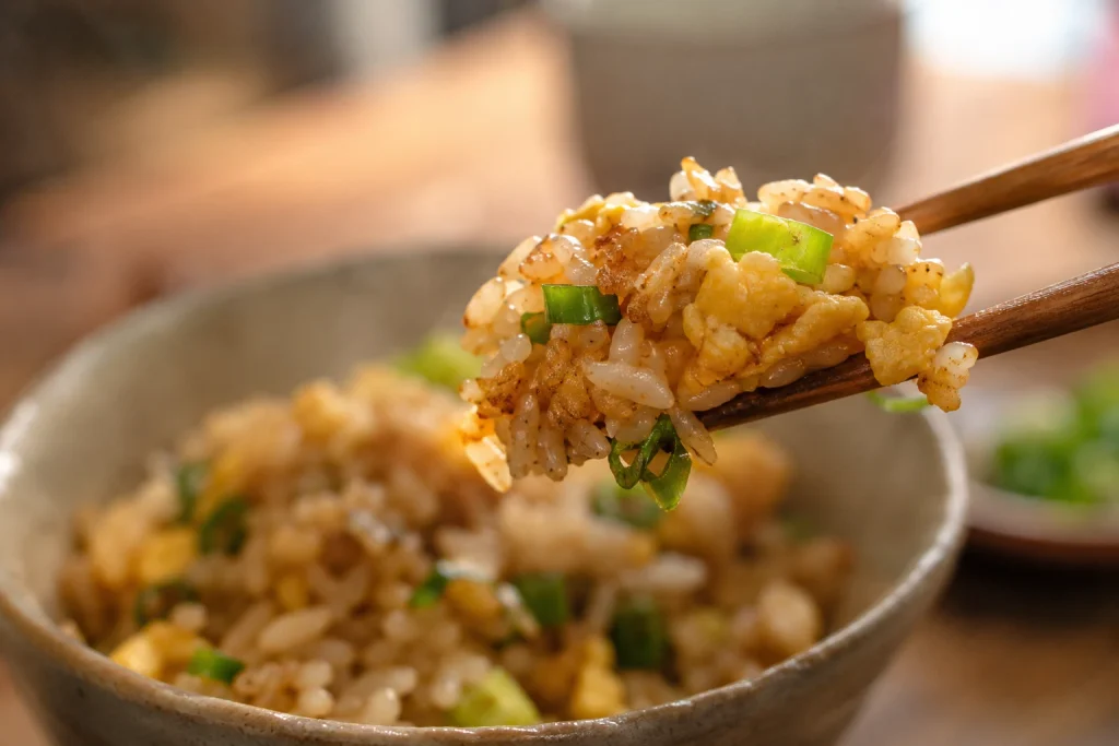 Chopsticks lifting a bite of quick fried rice recipe with egg curds and green onion