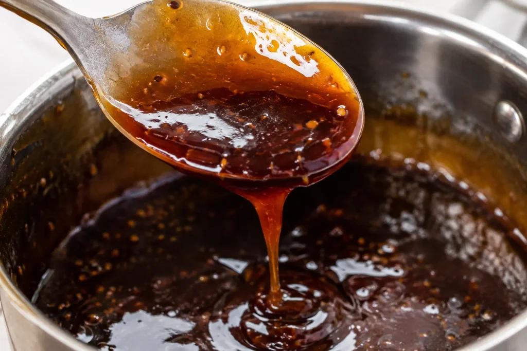 Spoon coated in thick glossy teriyaki glaze dripping back into pan
