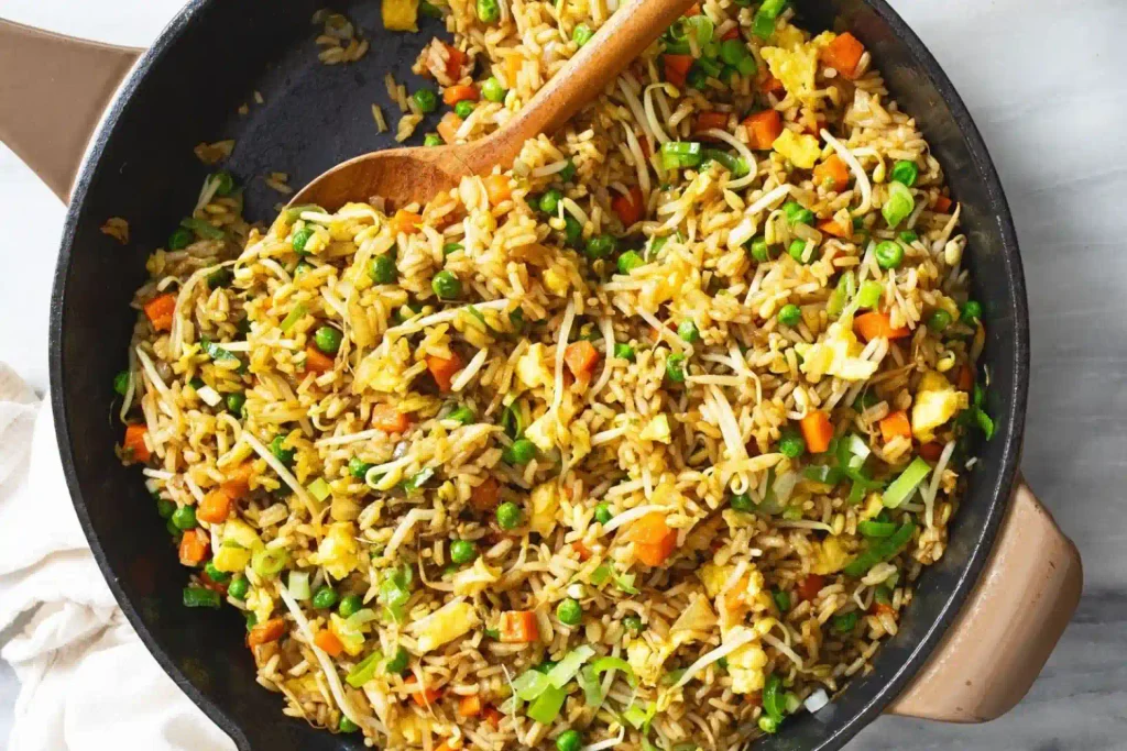 Homemade vegetable egg fried rice with peas, carrots, bean sprouts, green onions, and scrambled eggs in a cast iron skillet.