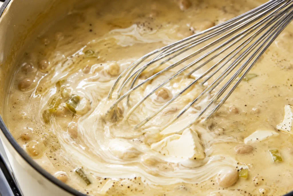 Whisk stirring cream cheese into creamy chicken chili broth